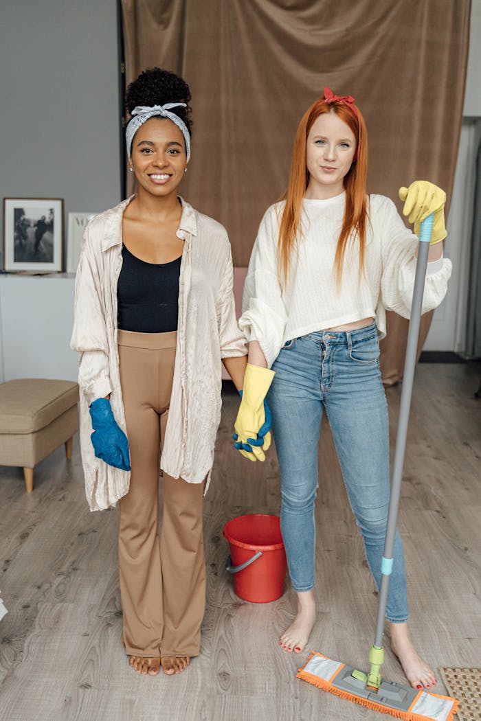 services-01 Two women smiling and holding hands while cleaning indoors, symbolizing teamwork.